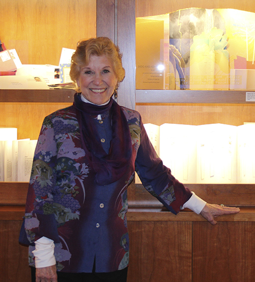 Cynthia Sears smiles as she stands in front of a well lit display case filled with handmade books.