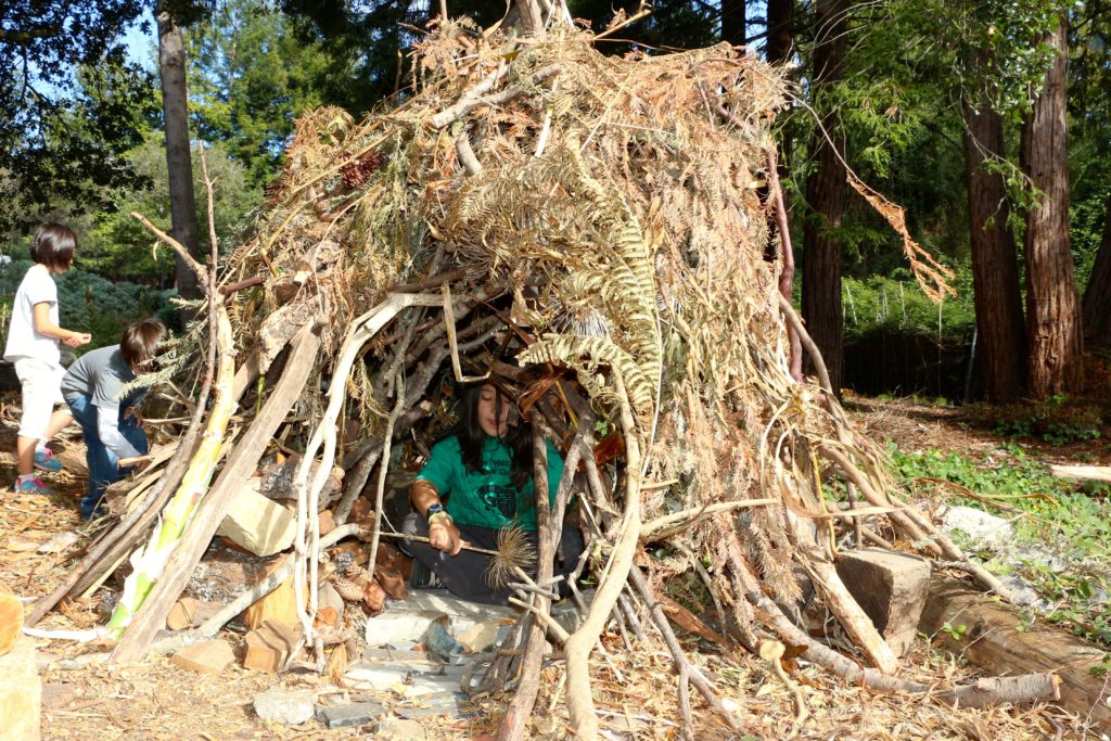 A child sits inside a den made in the Create-With-Nature Zone in Blake Garden, Kensington, California, 2013