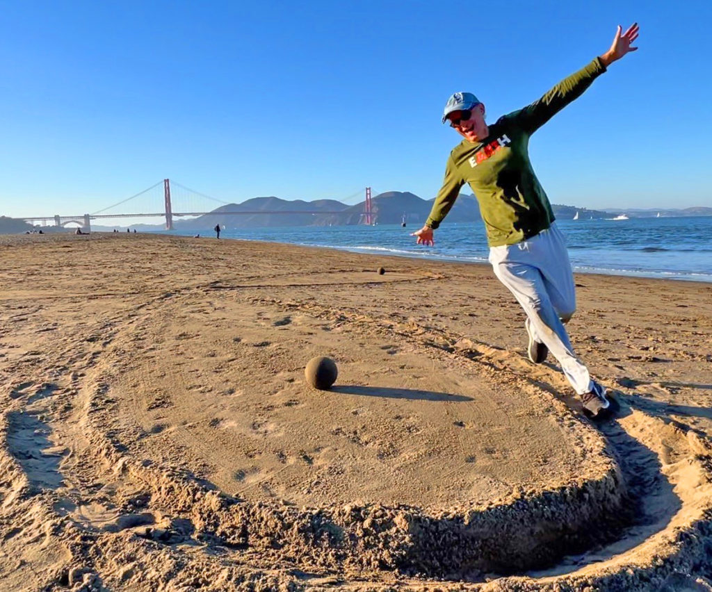 Zach running on a beach propeller with a sand globe decoration at Crissy Field East Beach, San Francisco.